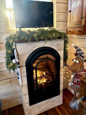 Une cheminée surmontée d’un téléviseur, un meuble en bois à droite et une décoration de Noël posée sur le manteau de la cheminée.