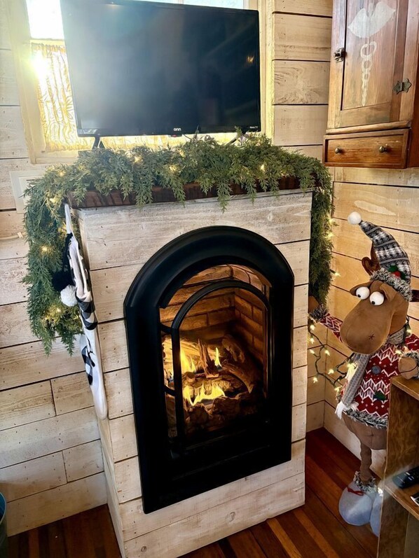 Une cheminée surmontée d’un téléviseur, un meuble en bois à droite et une décoration de Noël posée sur le manteau de la cheminée.