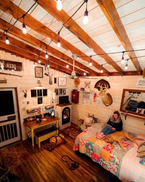 A cozy room with wooden beams, a fireplace, a bed with a colorful quilt, and various wall decorations including animal heads.