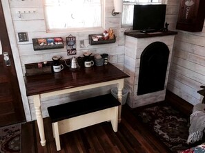 A compact kitchen with a wooden table, a coffee machine, and a television on a stand.