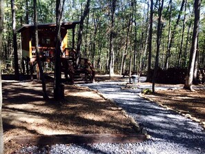 A cabin in a forest with a gravel path leading to it.