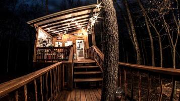 A wooden deck with a staircase leading to a building, surrounded by trees.