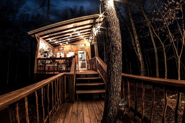 Une terrasse en bois avec un escalier menant à un bâtiment, le tout entouré d’arbres.