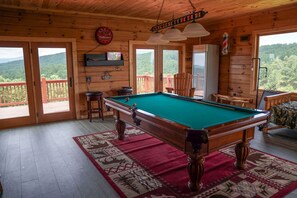 Une table de billard dans une pièce en bois, avec un tapis rouge, une horloge et un réfrigérateur.