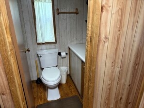 A compact bathroom with a toilet, a small trash bin, and a plunger.