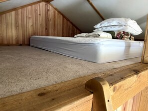 A small, single-bed room with a sloped ceiling and wooden walls.