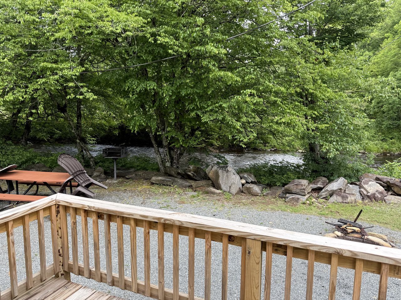 A wooden deck with a picnic table and chairs, surrounded by trees and a rocky area.