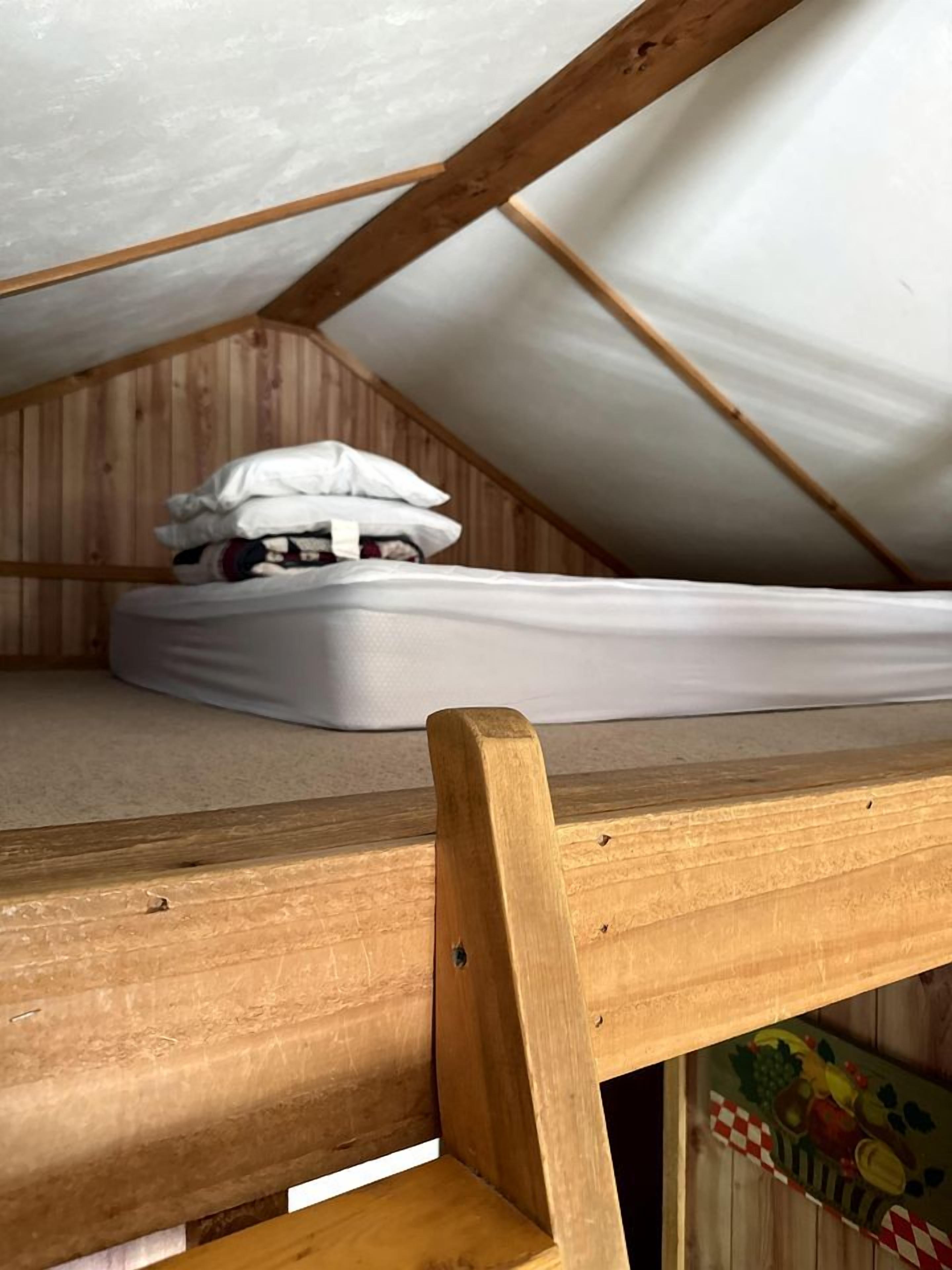 Ein kleines Schlafzimmer im Dachgeschoss mit einem Holzbett und einer Matratze auf dem Boden.