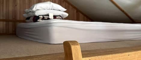 Ein kleines Schlafzimmer im Dachgeschoss mit einem Holzbett und einer Matratze auf dem Boden.
