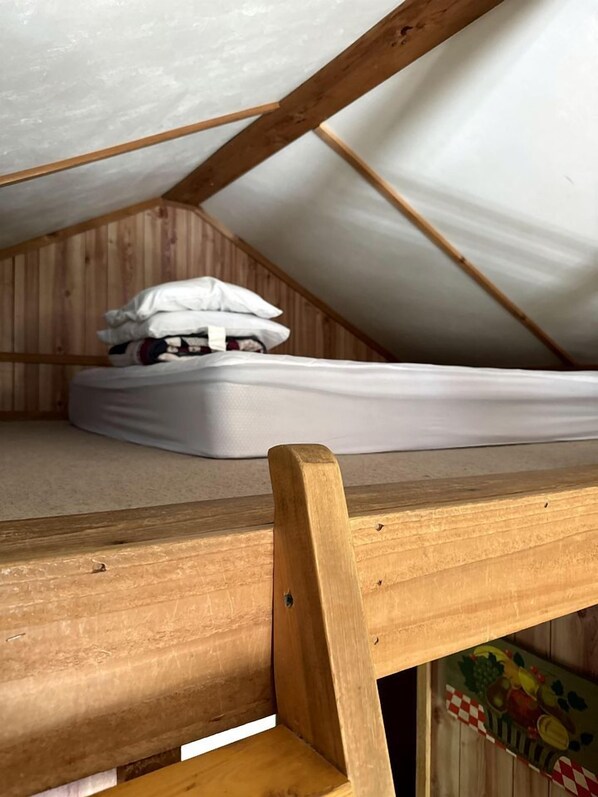 Un dormitorio abuhardillado pequeño con una cama nido de madera y un colchón en el suelo.