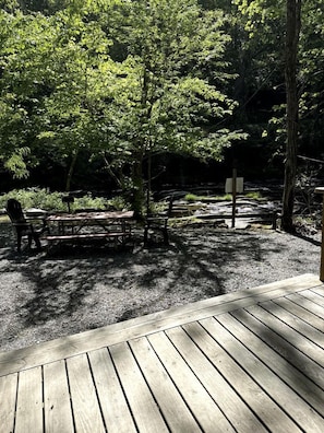 Une terrasse en bois avec une table de pique-nique et des chaises, entourée d’un feuillage verdoyant et luxuriant.
