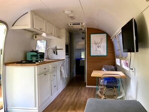 A compact kitchen with white cabinets, a microwave, and a small table with a chair.