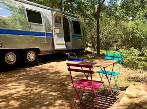 A campervan parked in a wooded area with a picnic table and chairs.