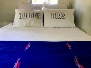 A bed with two pillows, one with 'BUENOS DÍAS' text.