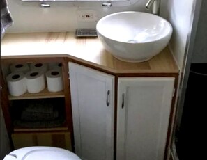 A small bathroom with a white sink, toilet, and cabinet containing toilet paper.