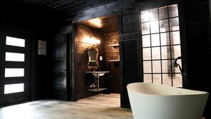 Un baño con una bañera independiente, un tocador con espejo y un aplique en la pared.