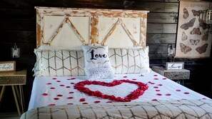 Una cama con un arreglo de pétalos de rosa en forma de corazón, un cojín con el texto 'Love' e ilustraciones de mariposas en la pared.