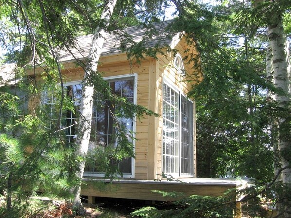 A wooden cabin with large windows, surrounded by trees.