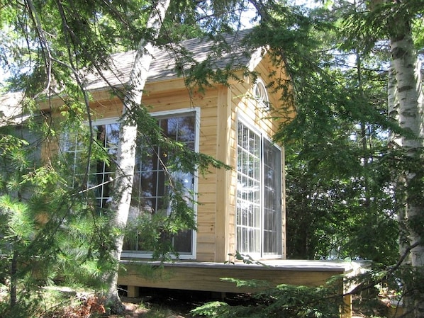 A wooden cabin with large windows, surrounded by trees.
