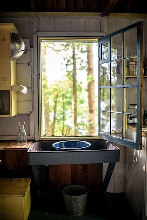 A rustic kitchen with a window, a sink, and a metal bucket.