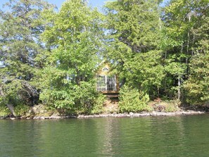 A secluded cabin surrounded by dense forest, a small dock extending into a calm lake, and a clear sky above.