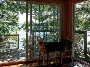 A wooden cabin with a glass door leading to a deck overlooking a lake.