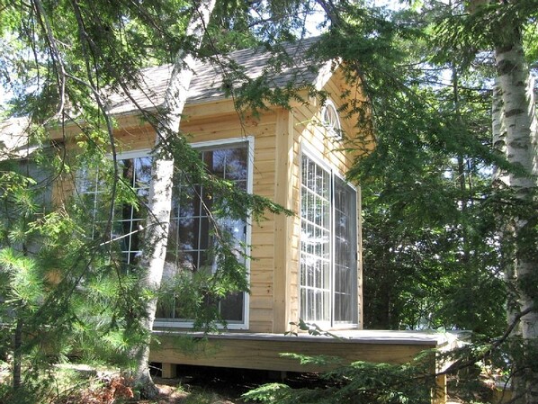A wooden cabin with large windows, surrounded by trees.