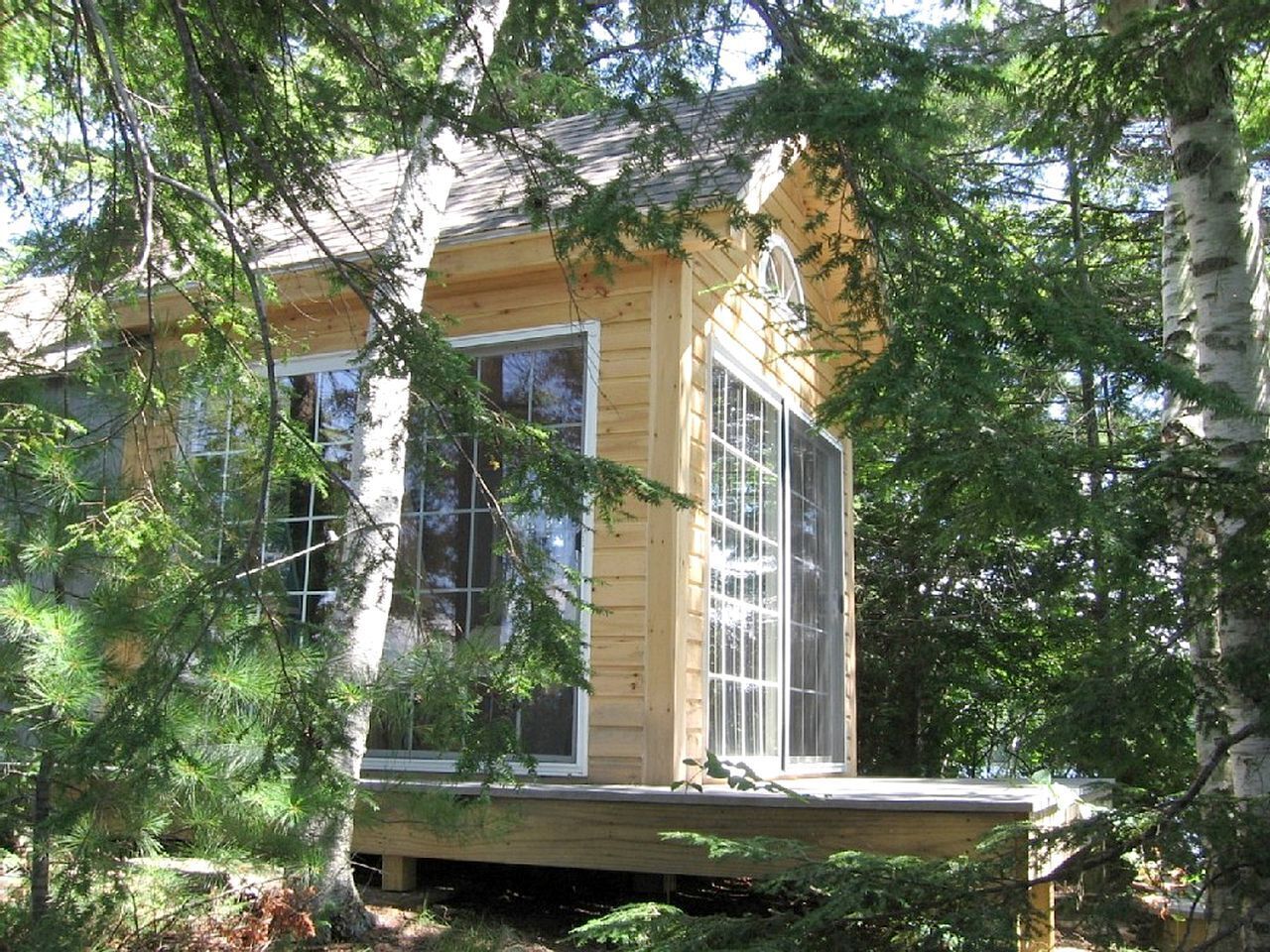 Une cabane en bois dotée de grandes fenêtres, entourée d’arbres.