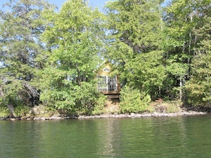 A secluded cabin surrounded by dense forest, a small dock extending into a calm lake, and a clear sky above.