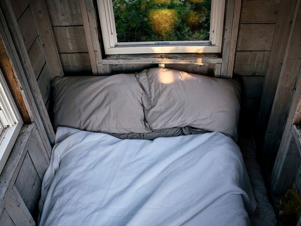 Ein kleiner, schmaler Raum mit einem Bett, einem Fenster und Holzwänden.