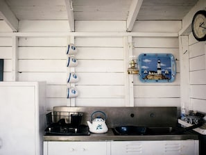 A kitchen with a stove, kettle, sink, and wall-mounted kettle. - Off-The-Grid Cottage Rental with Beautiful Views on Crow Island, Maine (Arrowsic)