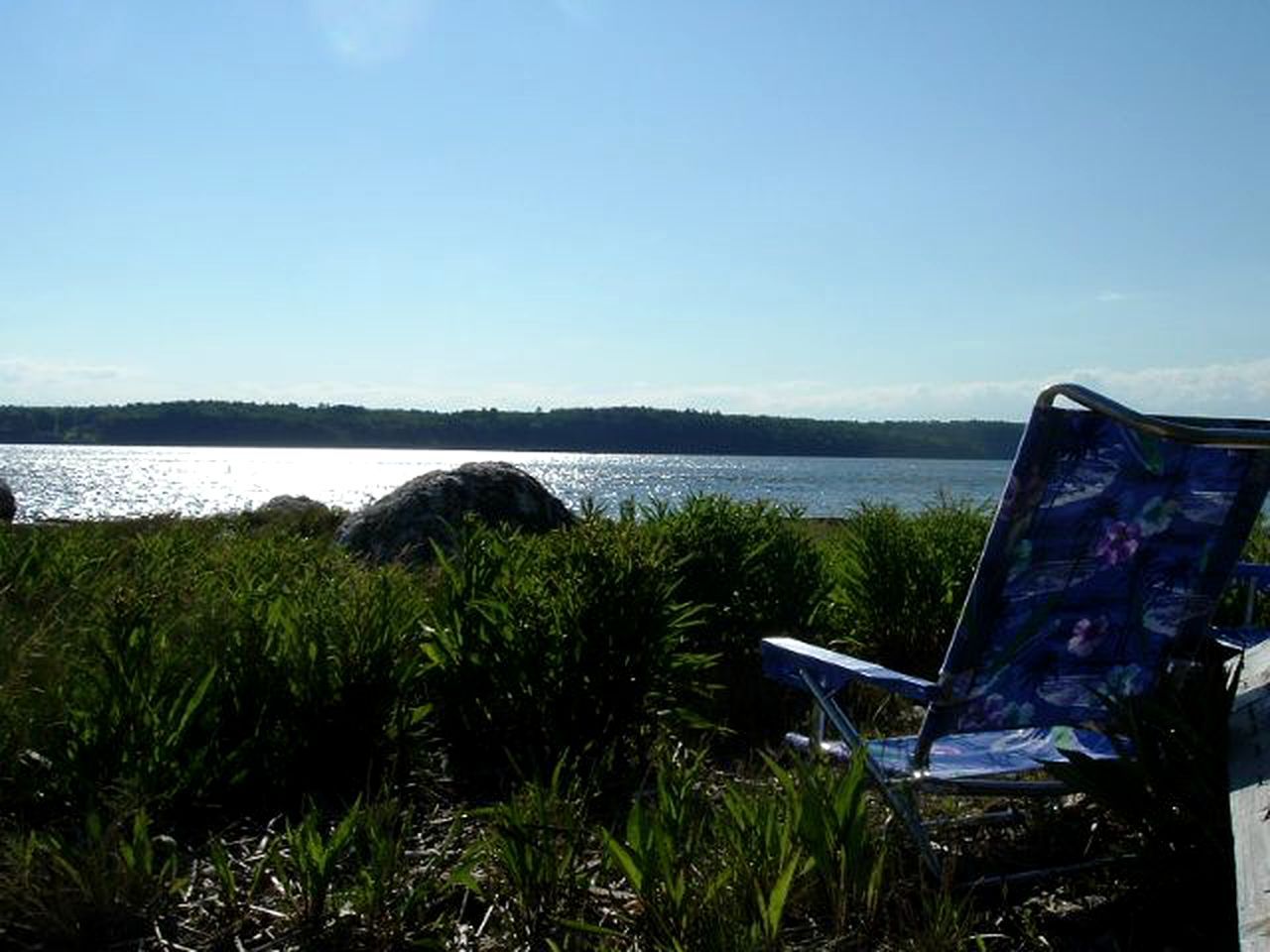 A chair by a lakeside with a clear view of the water and distant shoreline.