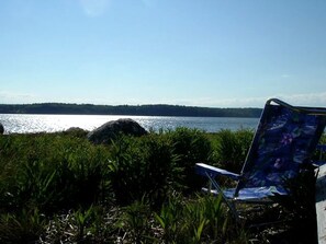 A chair by a lakeside with a clear view of the water and distant shoreline.