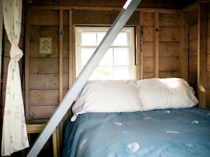 A wooden cabin room with a bed, a window, and a curtain.
