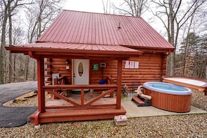 A wooden cabin with a hot tub, a covered porch, and a door.