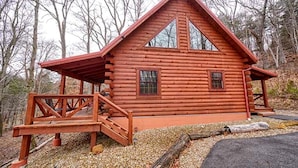 A log cabin with a porch, a staircase, and a window.