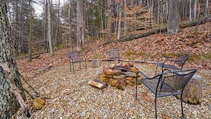 A forest setting with a fire pit, chairs, and a stone wall. - Rustic Log Cabin Escape in Logan, Ohio, with Hot Tub and Infrared Sauna (Logan)
