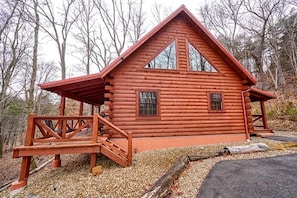 A log cabin with a porch, a staircase, and a window.