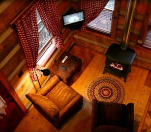 Ein gemütliches Blockhauss-Interieur mit einer Couch, einem kleinen Tisch, einem Fernseher, einem Kamin und einem gemusterten Teppich.