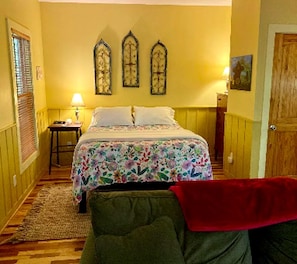 Ein Schlafzimmer mit Bett, Nachttisch, Lampe, Fenster mit Jalousien und einer Tür.
