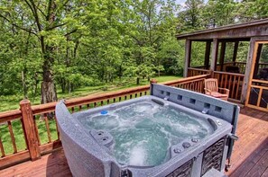 A hot tub on a wooden deck with a wooden railing, surrounded by trees.