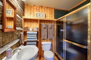A wooden bathroom with a sink, toilet, and a glass shower enclosure.