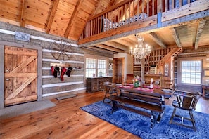 A rustic interior with wooden beams, a chandelier, a dining area with a bench, and a fireplace.