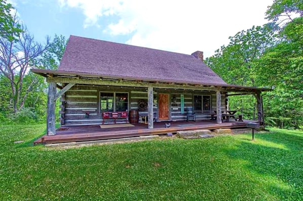 A log cabin with a porch, a picnic table, and a bench.