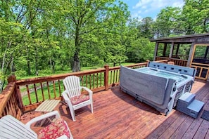 A wooden deck with a hot tub, two Adirondack chairs, and a gazebo.