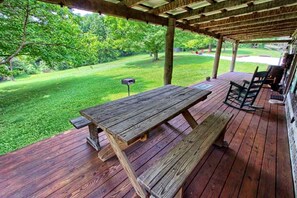 A wooden deck with a picnic table and chairs, surrounded by a grassy lawn and trees.
