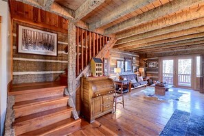 A rustic interior with wooden floors, a staircase, a wooden cabinet, a sofa, and a television.