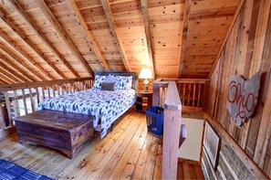 Una camera da letto in stile loft con soffitto in legno, un letto con biancheria a motivi, un comodino con una lampada e un cartello appeso al muro.