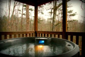 Een hottub in een houten gazebo met uitzicht op een bos.