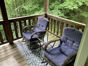 A wooden deck with wicker chairs and a glass table. - Secluded Woodland Cabin Rental with Hot Tub in Yadkin Valley Wine Region (Elkin)